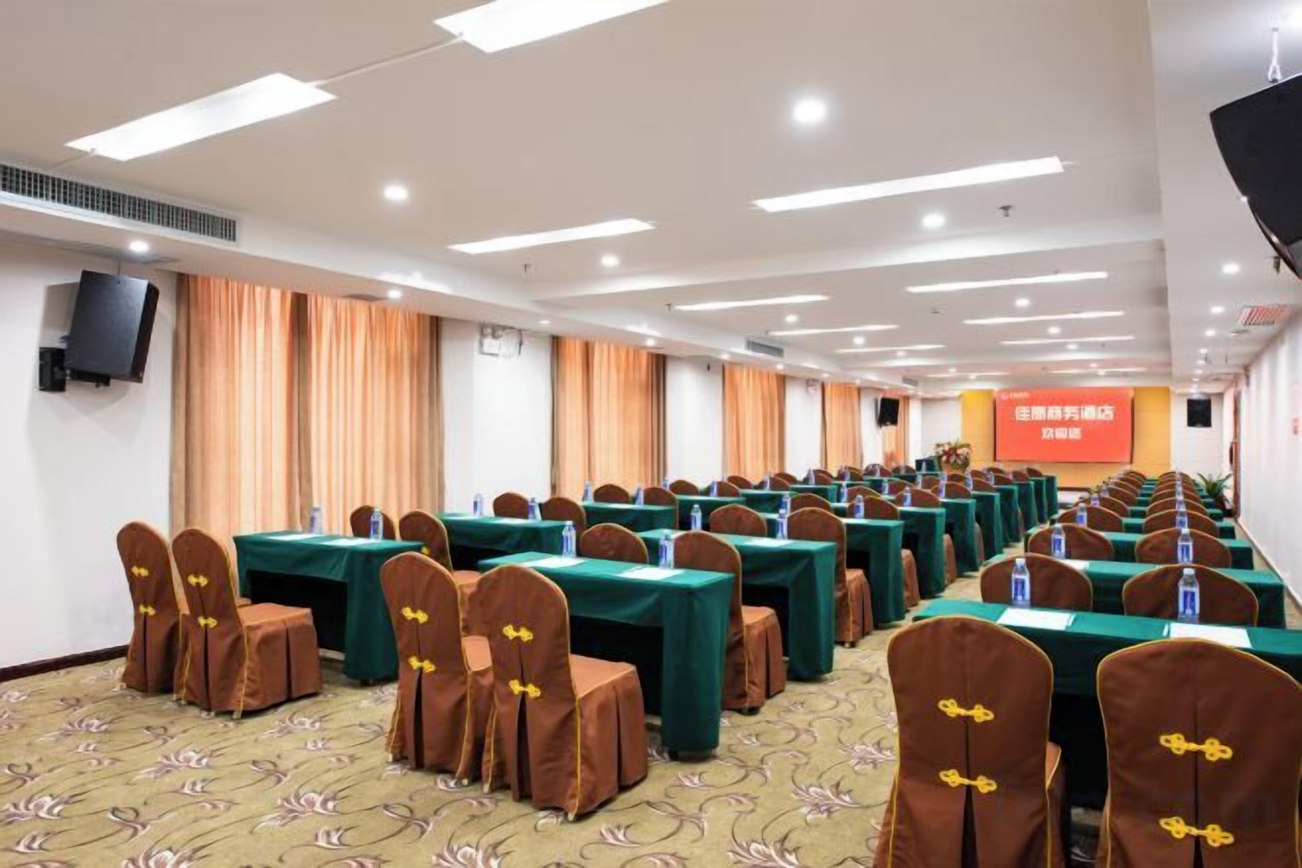 A conference room with rows of tables and chairs, a stage with a screen, and a red banner with text.