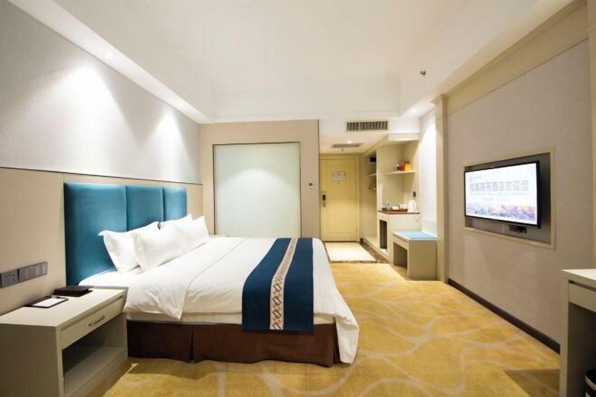 A hotel room with a bed, bedside table, TV, and a door leading to a bathroom.