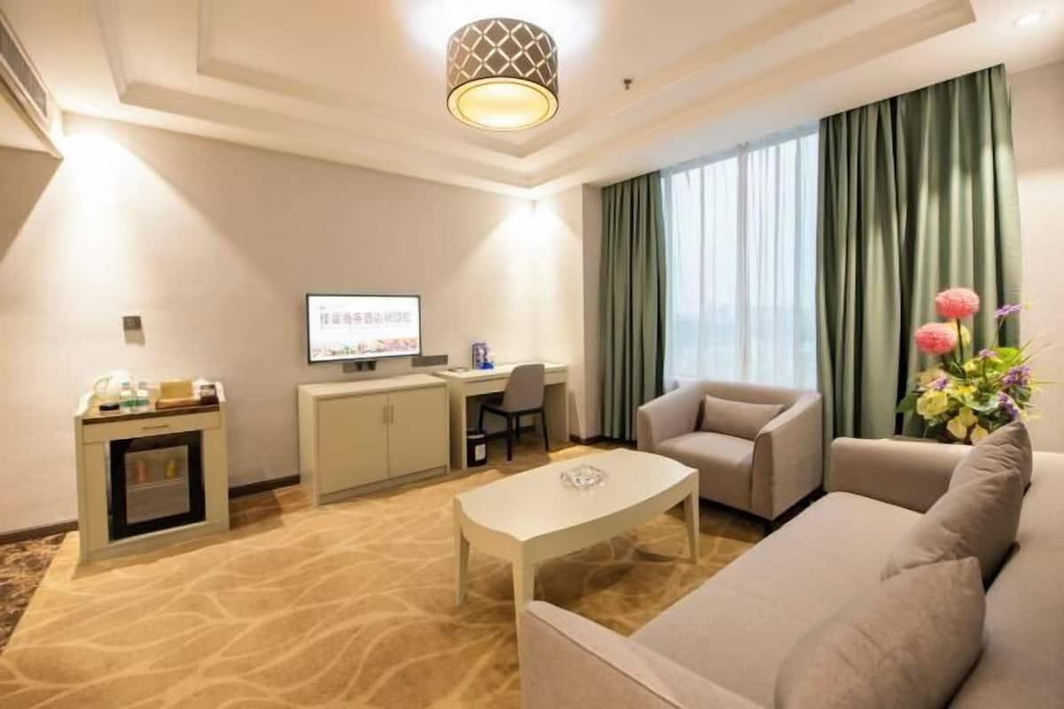 Een hotelkamer met een bank, een klein tafeltje, een bureau met een computer, een televisie en een decoratieve vaas.