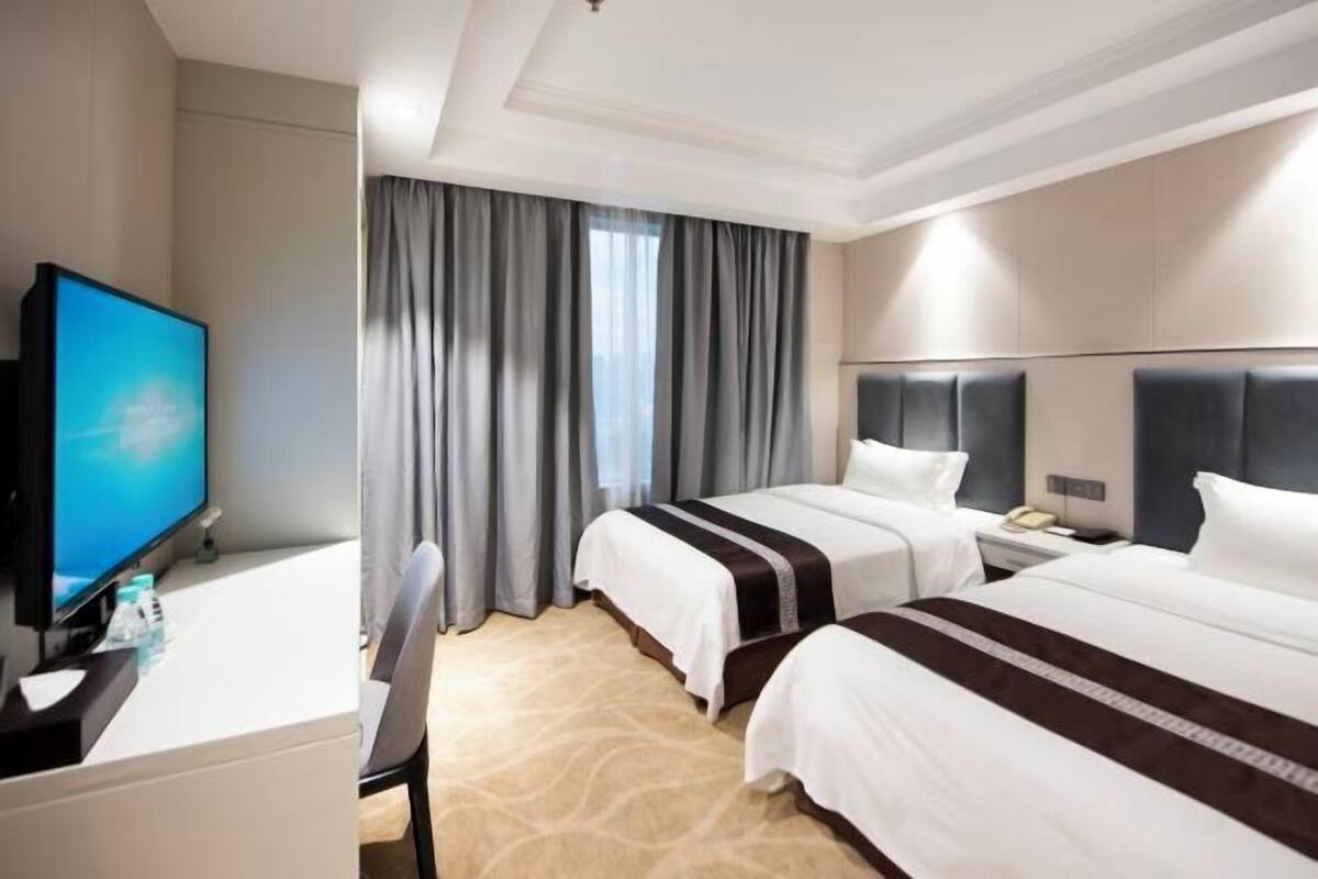 Een hotelkamer met twee bedden, een bureau met een televisie en een raam met gordijnen.