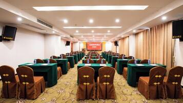 A conference room with rows of tables and chairs, a stage with a screen, and a carpeted floor.