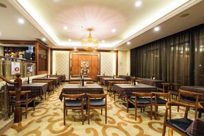 A restaurant with multiple tables and chairs, a chandelier, and a patterned carpet.