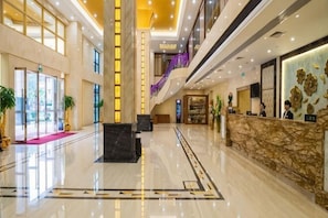 A spacious lobby with a reception desk, a staircase, and a large window.