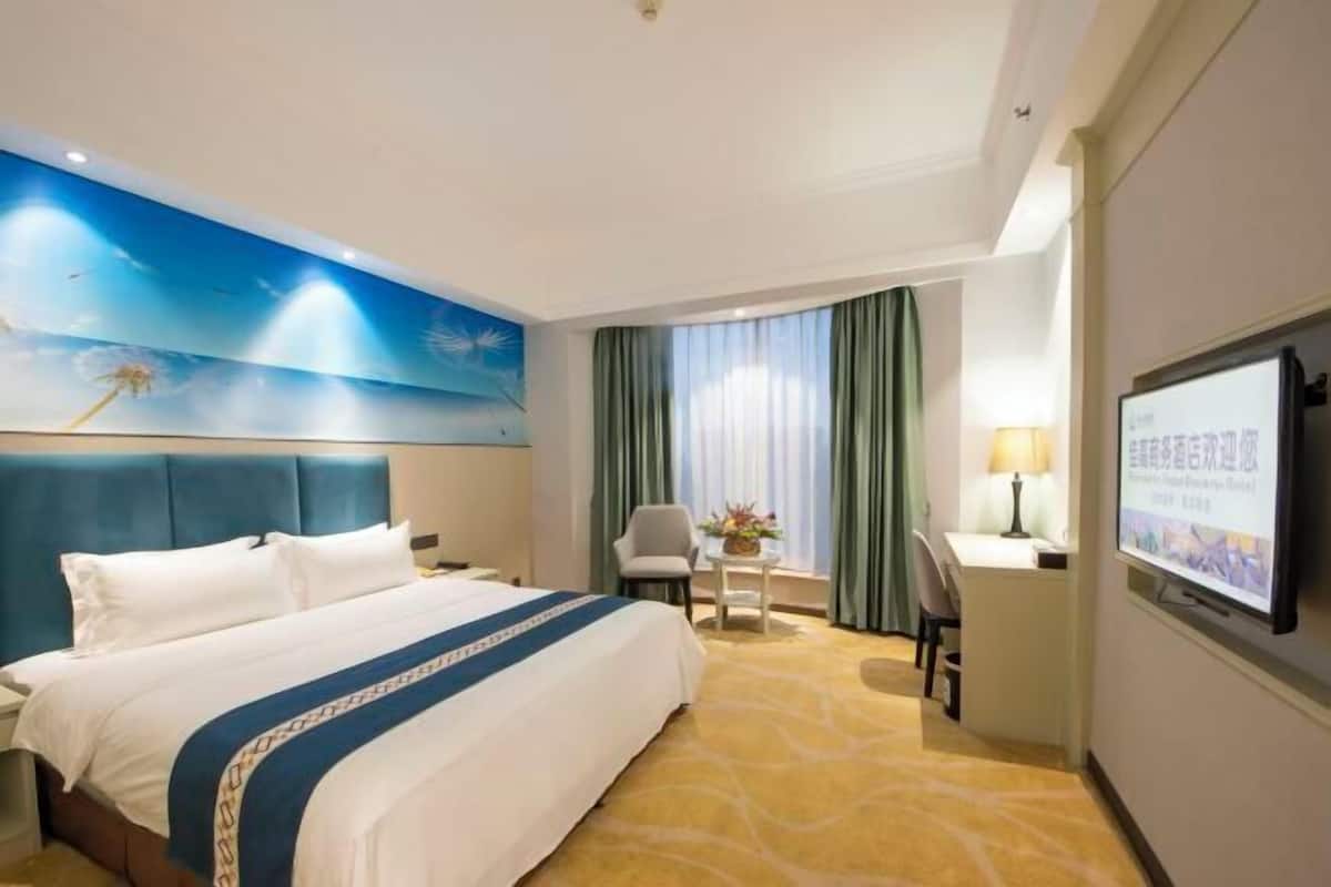 Een hotelkamer met een bed, een bureau, een stoel, een televisie en een wandgemonteerd scherm.