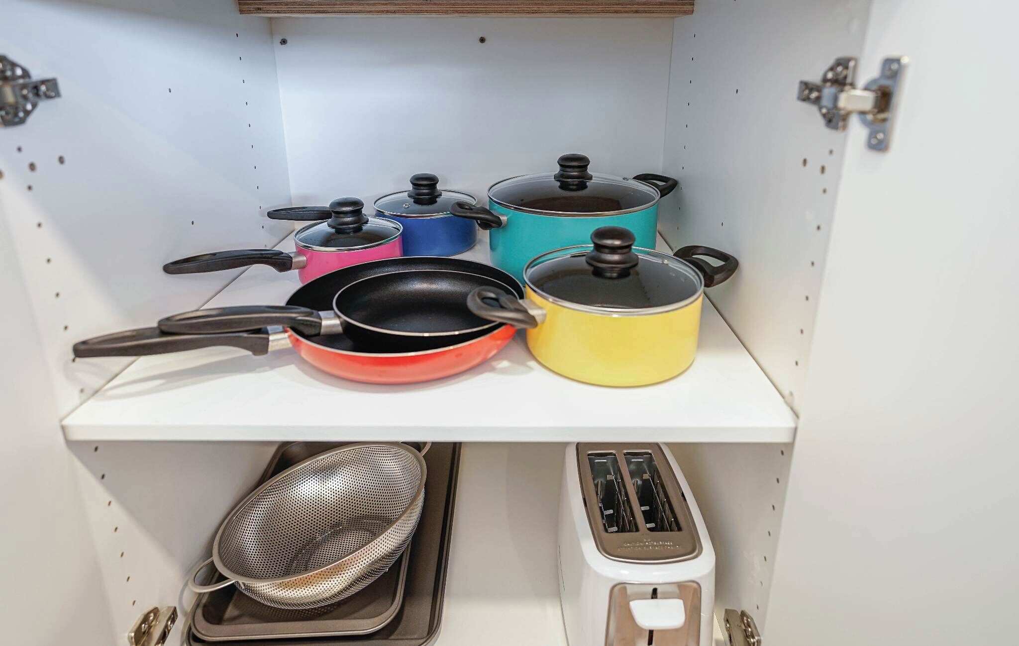 Una cocina con ollas, sartenes, un colador y un tostador.