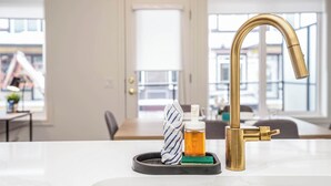 A kitchen counter with a gold faucet, a towel, and a bottle of hand soap. - NEW Home, Double Car Garage & Close to Airport (Calgary)