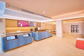 Een receptiegedeelte van een hotel met een modern design, met een receptiebalie, een digitaal scherm en een zithoek.