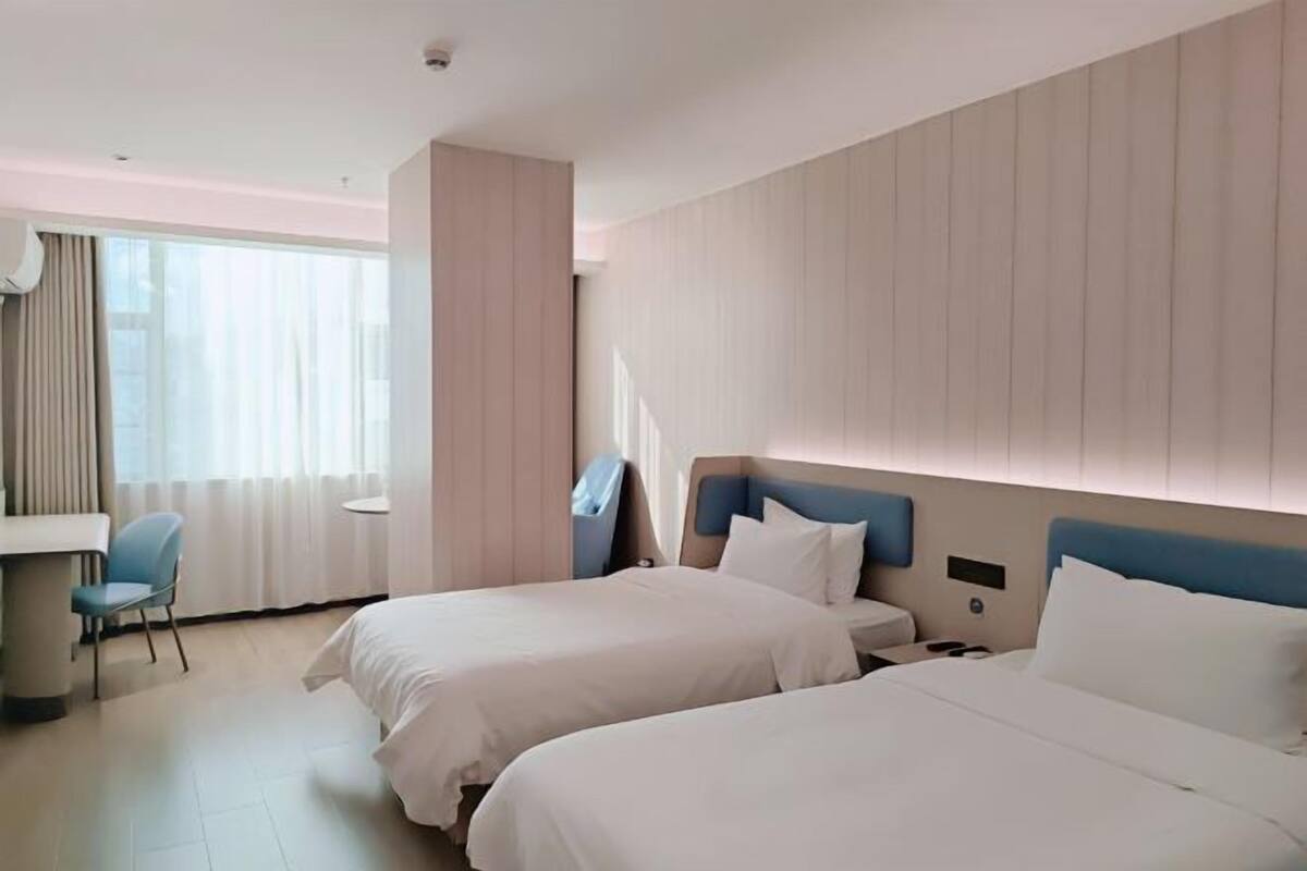 Hotellihuone, jossa on kaksi sänkyä, työpöytä, tuoli ja suuri ikkuna, jossa on verhot.