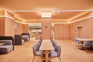 Een moderne hotellobby met een lange eettafel, comfortabele zitplaatsen en een bar op de achtergrond.