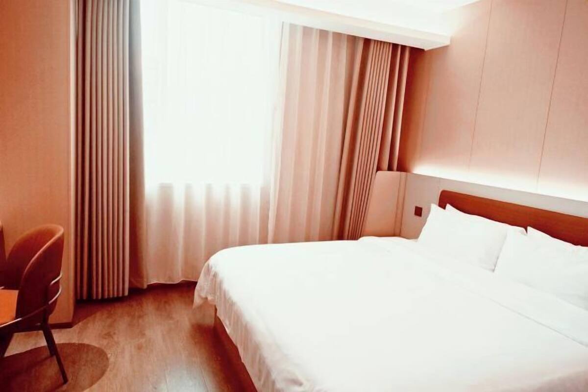 Hotellihuone, jossa on sänky, tuoli ja ikkuna, jossa on verhot.