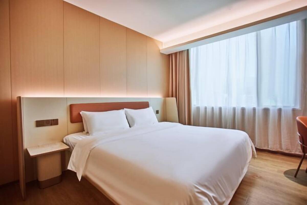 Hotellihuone, jossa on suuri sänky, yöpöytä, tuoli ja ikkuna, jossa on verhot.