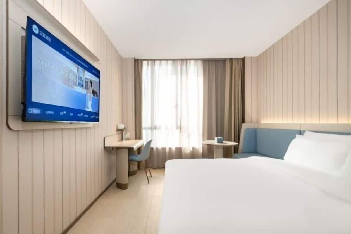 Hotellihuone, jossa on sänky, työpöytä, tuoli, seinälle asennettu televisio ja ikkuna, jossa on verhot.