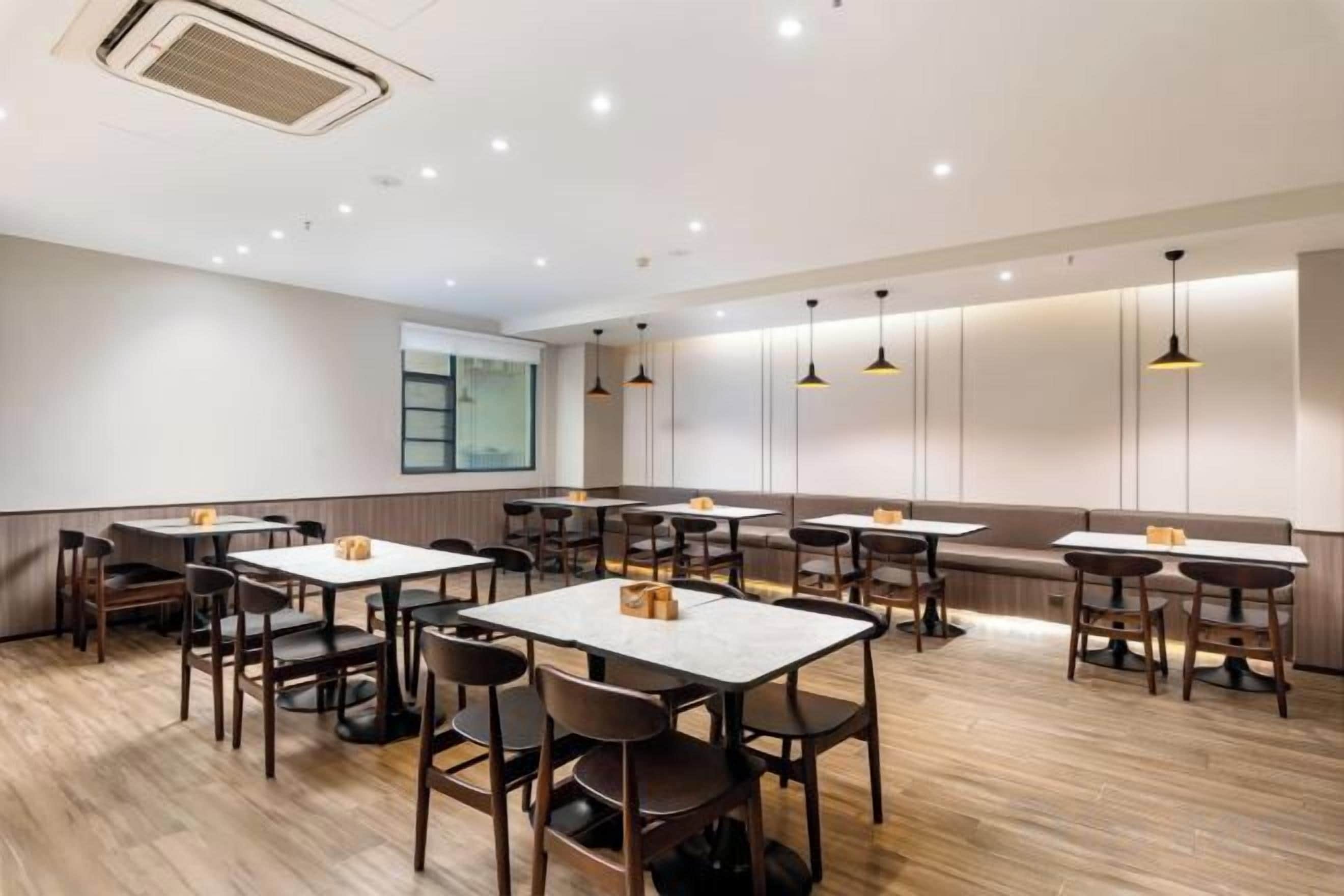 A restaurant with multiple tables and chairs, a wooden floor, and pendant lighting.