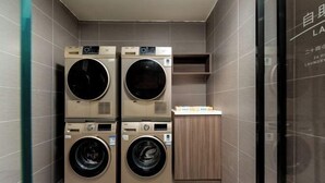 Une buanderie équipée de quatre machines à laver superposées, d’un meuble en bois et d’un mur carrelé.