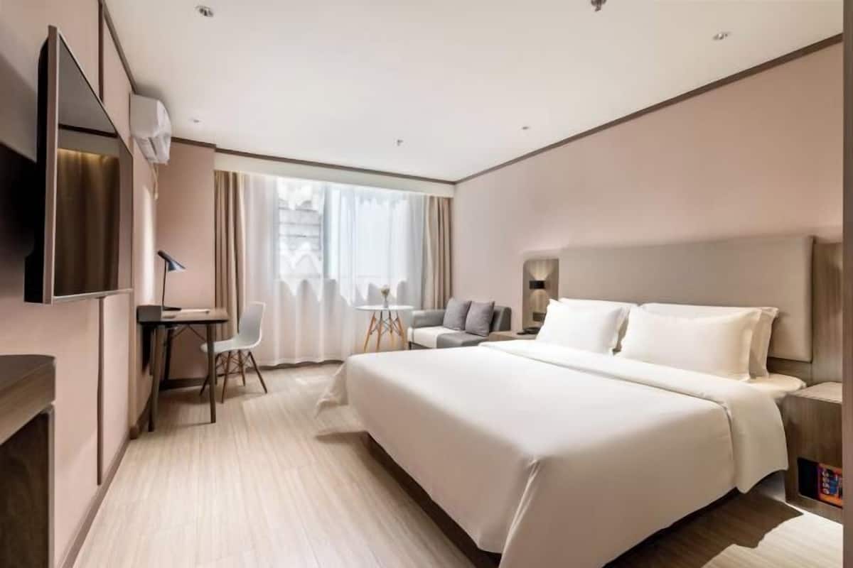 A modern hotel room with a large bed, a desk, a chair, and a sofa.