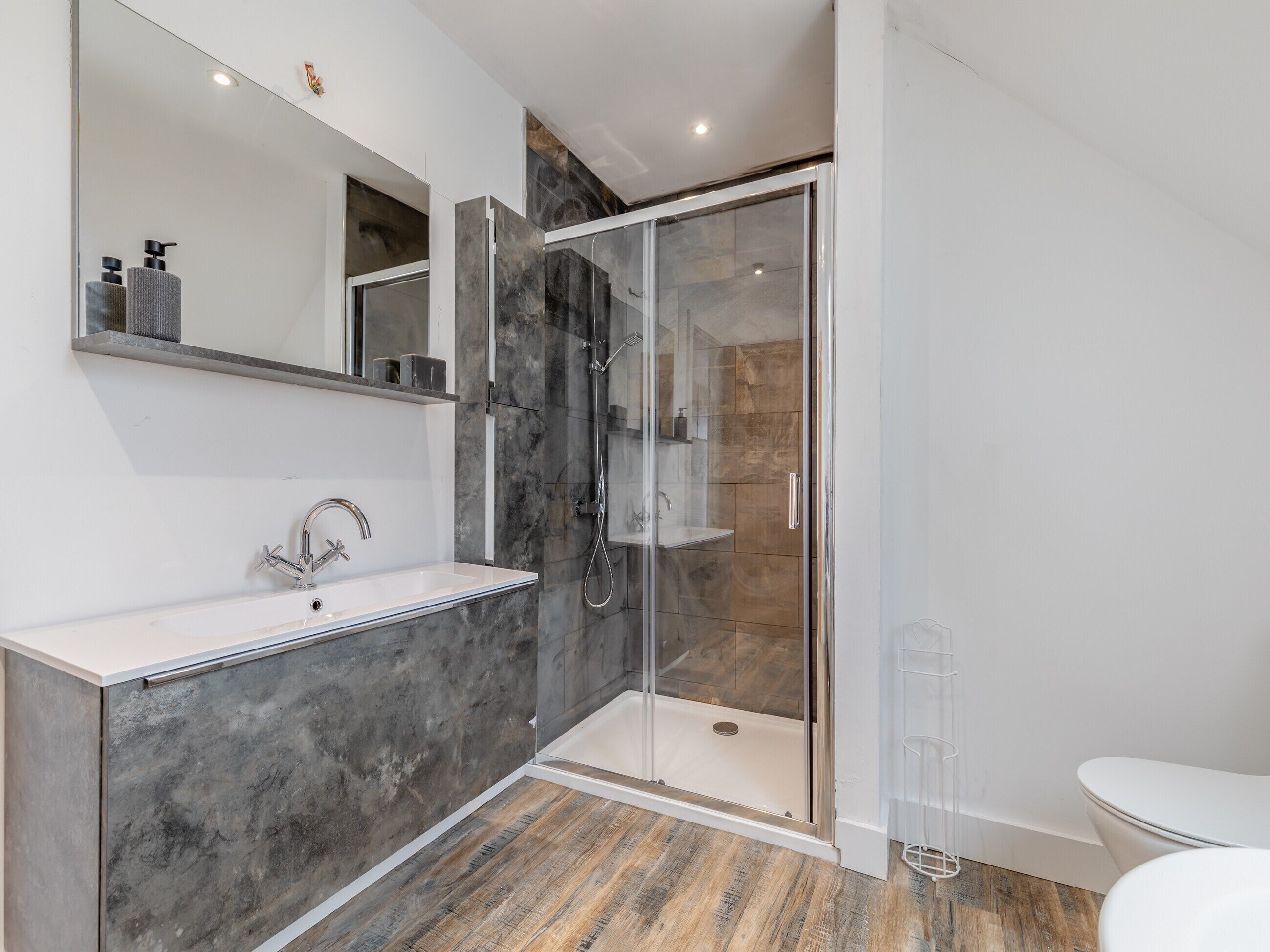 Un baño moderno con ducha de vidrio, lavabo blanco y un espejo grande.