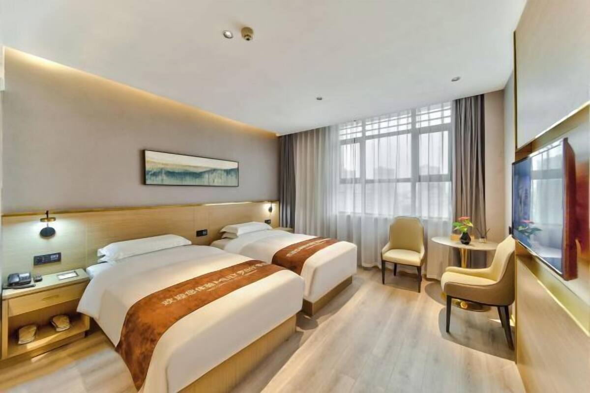 A hotel room with two beds, a desk, a chair, a TV, and a window with curtains.