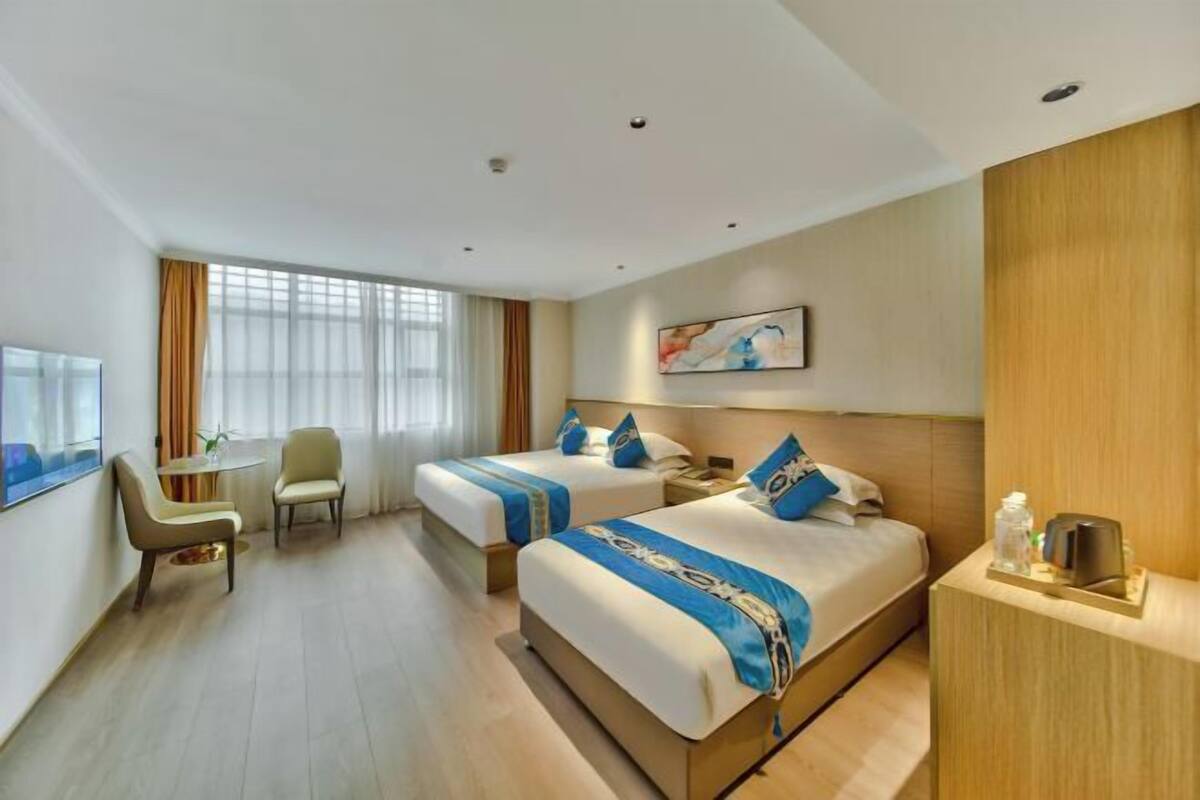 A hotel room with two beds, a desk, a chair, and a TV.