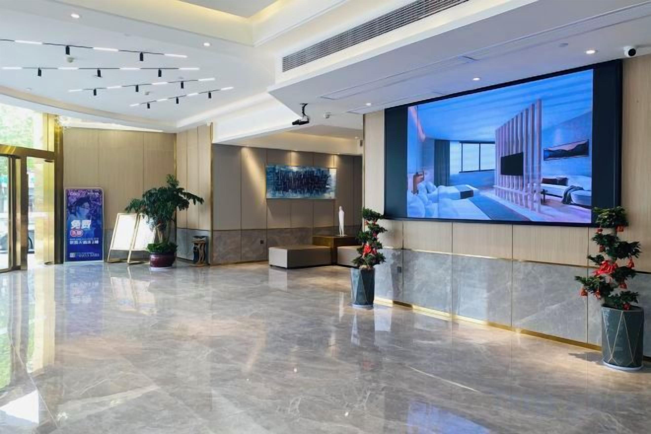 En rymlig entréhall med en stor digital skärm, en receptionsdisk och krukväxter.