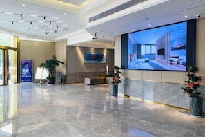 A spacious lobby with a large digital display, a reception desk, and potted plants. - Oukai Hotel (Hangzhou)