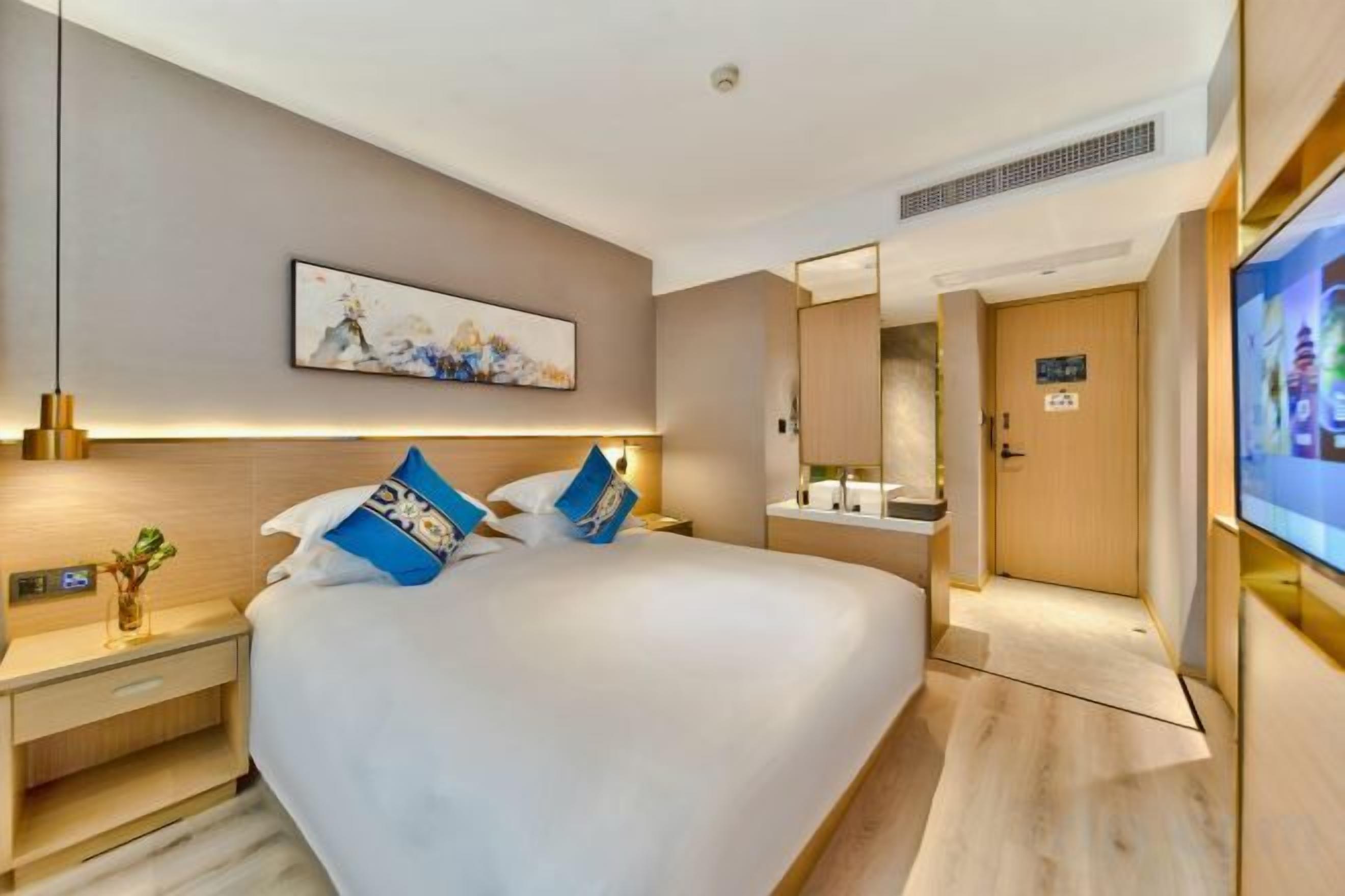 Quarto de hotel com cama grande, mesas de cabeceira, televisão de tela plana, espelho e porta com placa.