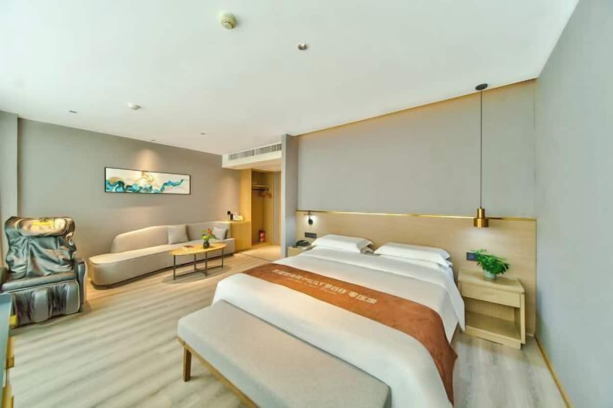 A modern hotel room with a large bed, a sofa, a chair, and a small table.