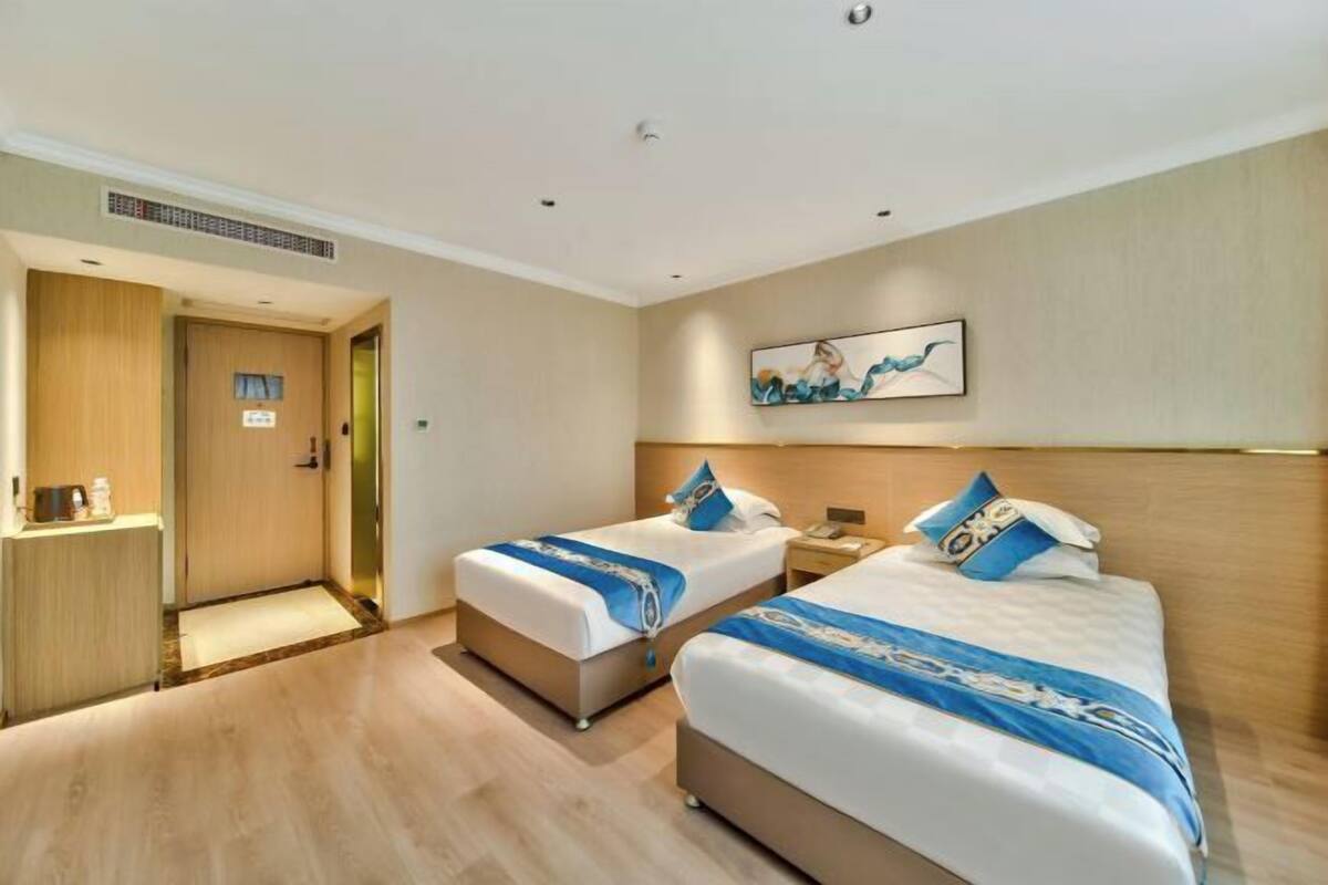 A hotel room with two beds, a wooden headboard, a painting on the wall, and a small desk with a lamp.