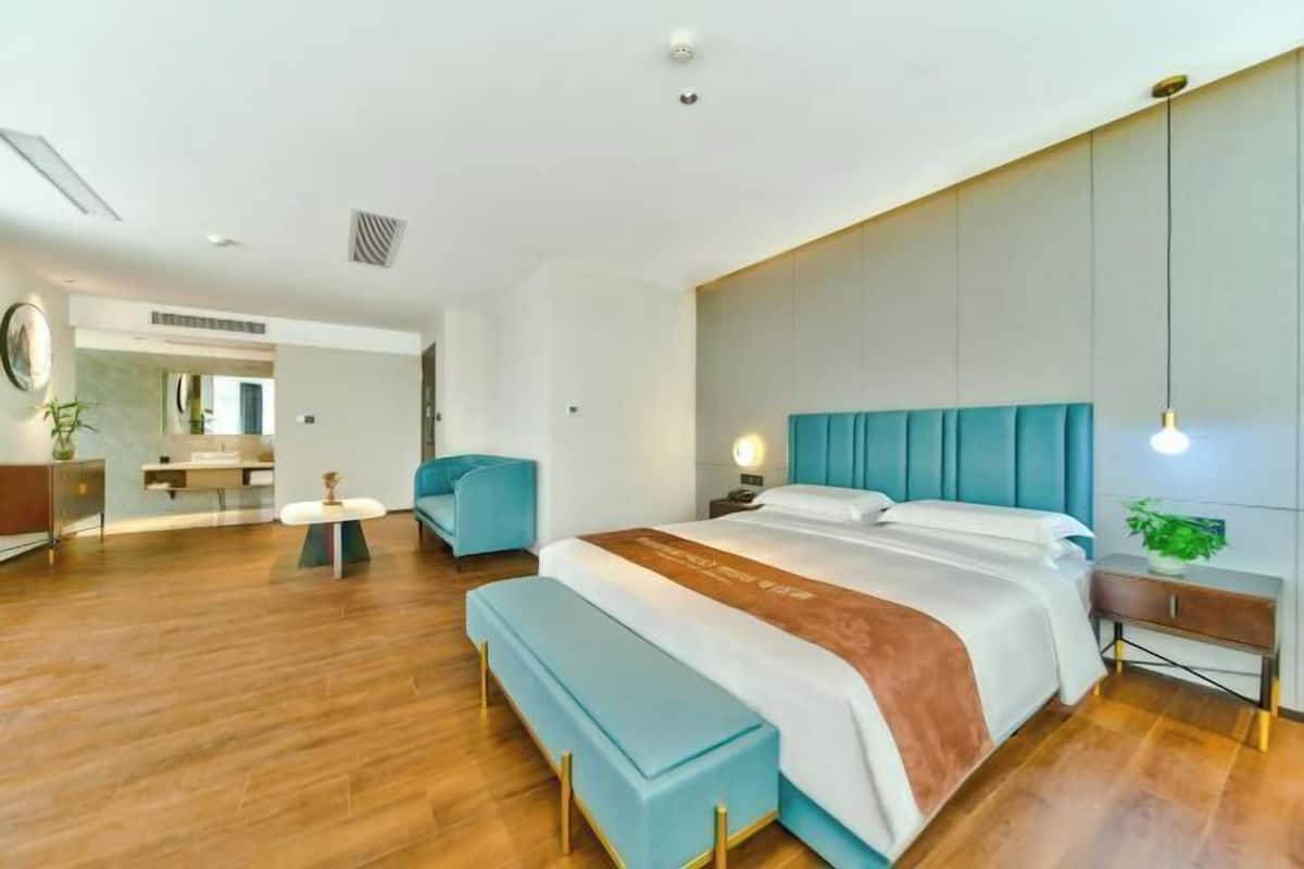 A modern hotel room with a large bed, a bench, a bedside table, and a nightstand.