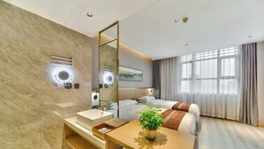 A modern hotel room with a large bed, a bedside table with a plant, a mirror, and a bathroom with a sink and vanity. - Oukai Hotel (Hangzhou)