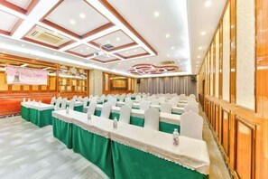 Un salón de conferencias con filas de mesas, un escenario y una pared de paneles de madera.