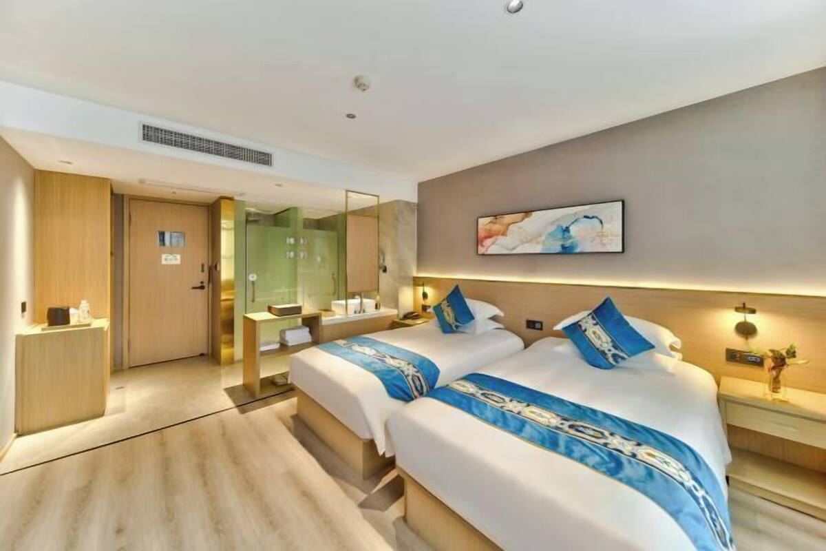 A hotel room with two beds, a large mirror, a painting on the wall, and a small desk with a lamp.