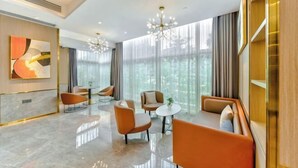A modern hotel lobby with a marble floor, orange seating, a chandelier, and large windows. - Oukai Hotel (Hangzhou)