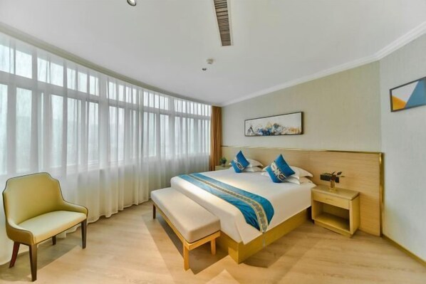 A hotel room with a large bed, a bench, a bedside table, and a window with curtains.