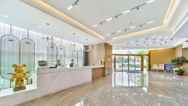 A modern hotel reception area with a marble floor, a reception desk, and a large golden bear sculpture. - Oukai Hotel (Hangzhou)