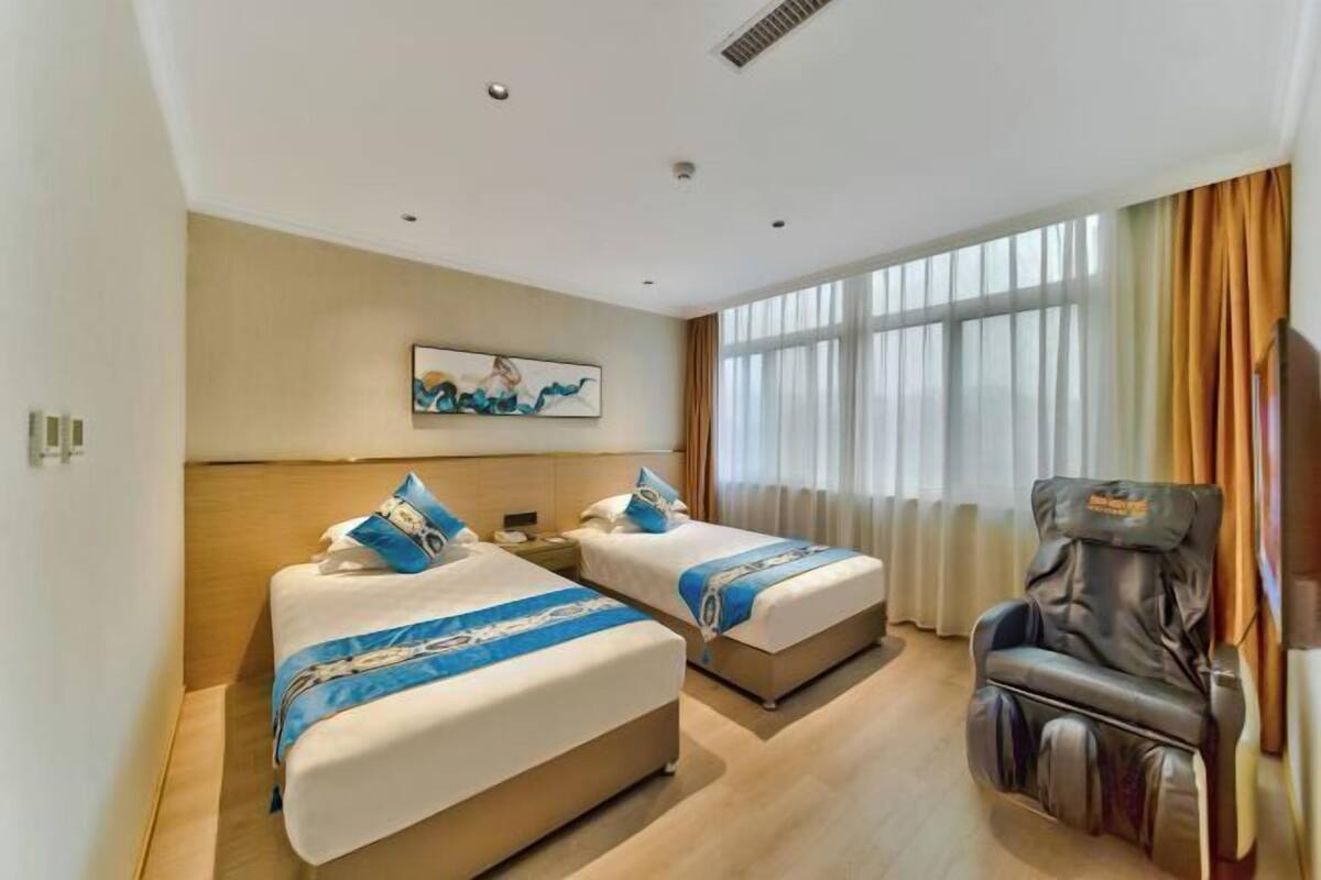 A hotel room with two beds, a massage chair, and a large window with curtains.