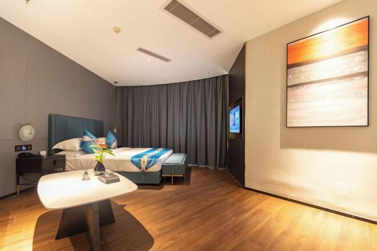 A hotel room with a bed, bedside table, TV, and a painting on the wall.