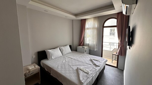 Quarto de hotel com cama, mesa de cabeceira e uma pequena mesa com telefone.
