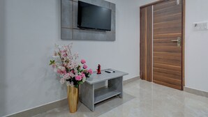 A modern room with a mounted TV, a small console table, a vase with flowers, and a wooden door. - Hotel Cloud 9 Luxury stay - Mysore (Mysore)