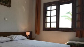 A neatly made bed with white linens, a bedside lamp, and a window with a view of greenery outside. - SANTA CATALINA (Polygyros)
