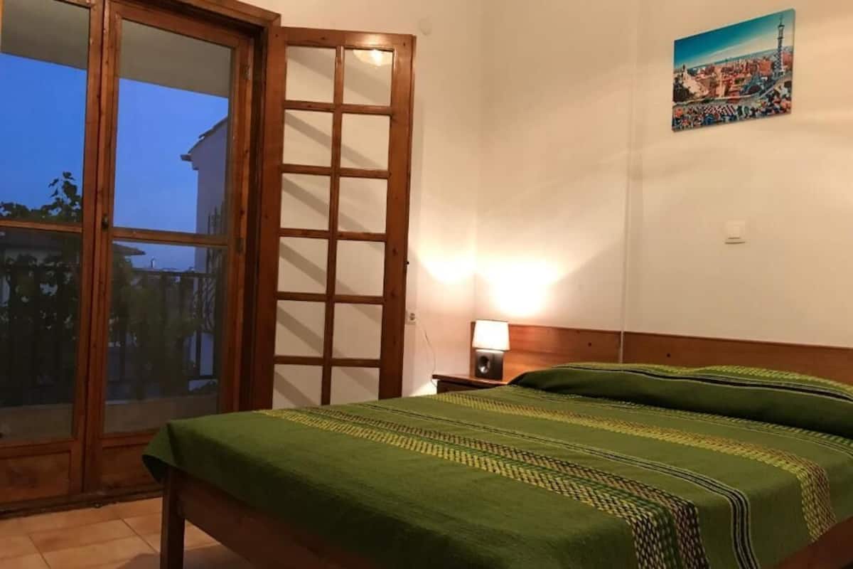 A bedroom with a bed, a nightstand, a lamp, and a sliding glass door leading to a balcony.