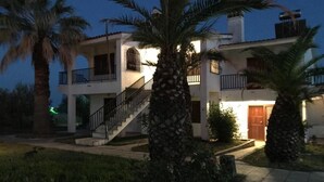 A two-story building with a balcony on the upper floor, surrounded by palm trees and a paved walkway. - SANTA CATALINA (Polygyros)