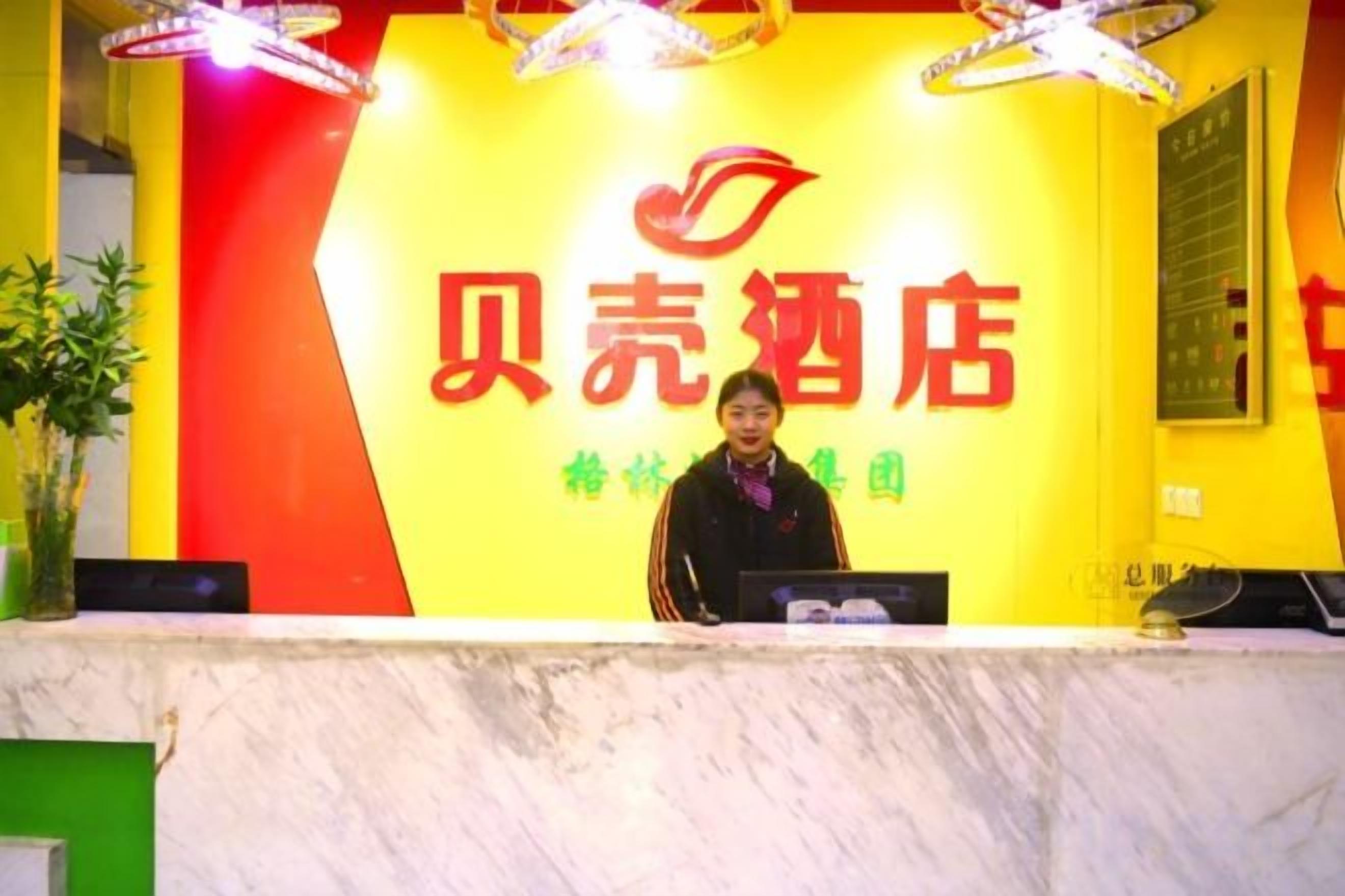 Een receptiebalie met een bord waarop '贝壳酒店' staat, en een vrouw die erachter staat.