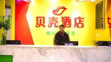 Een receptiebalie met een bord waarop '贝壳酒店' staat, en een vrouw die erachter staat.