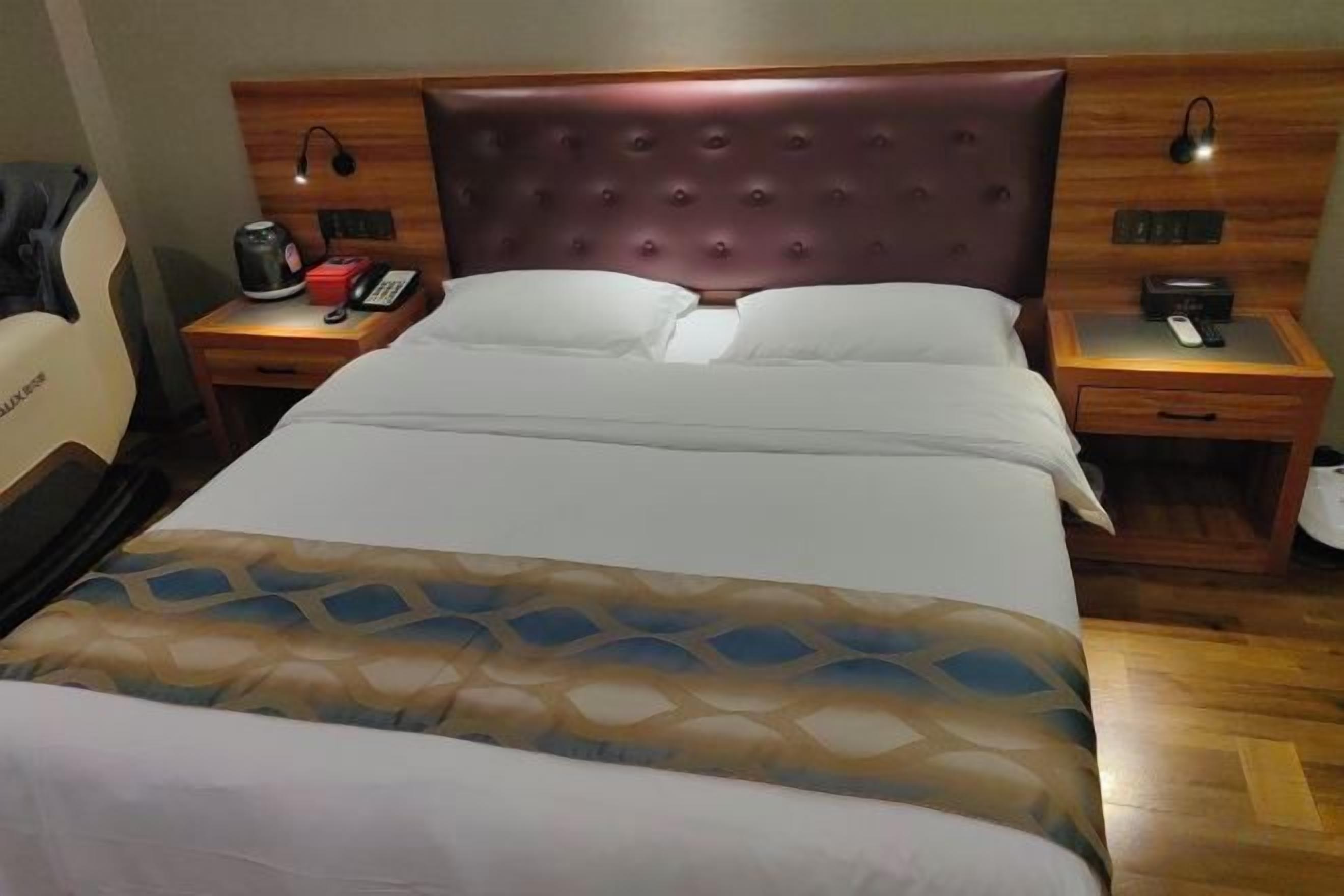 Habitación de hotel con una cama grande, un cabecero de madera, dos mesitas de noche con lámparas y una silla.