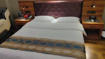 A hotel room with a large bed, a wooden headboard, two bedside tables with lamps, and a chair.