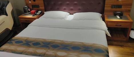Habitación de hotel con una cama grande, un cabecero de madera, dos mesitas de noche con lámparas y una silla.