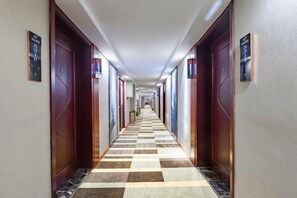 A hotel hallway with checkered flooring, wooden doors, and signs indicating room numbers. - Shell Hotel (Hefei Maanshan Road Hegongda Subway Station) (Hefei)