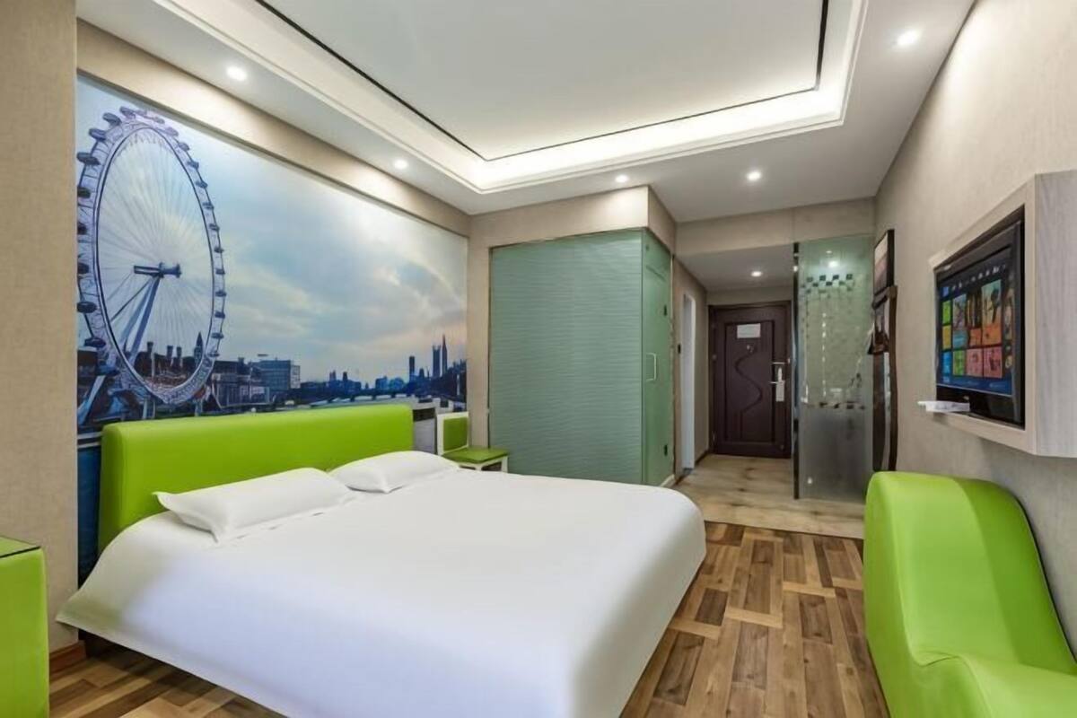 A hotel room with a bed, a green chair, a wardrobe, and a wall with a Ferris wheel mural.