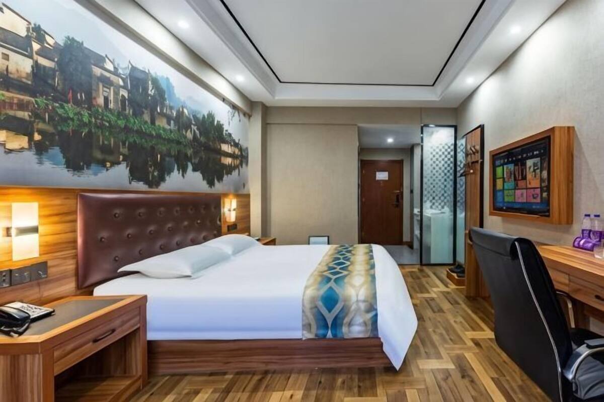 A hotel room with a bed, bedside table, desk, chair, and a wall-mounted TV.