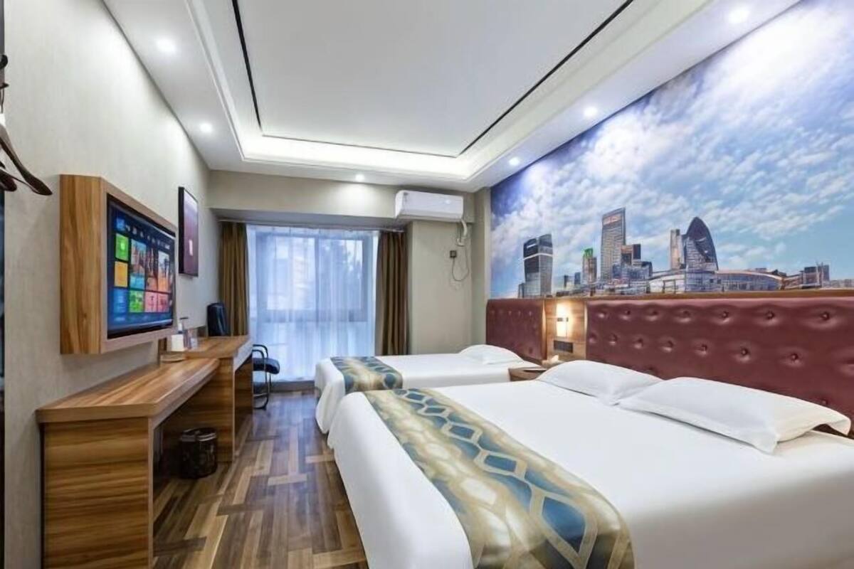 A hotel room with two beds, a desk, a TV, and a cityscape mural on the wall.